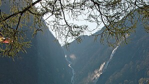 Une rangée de petites cabanes, avec une chaîne de montagnes en arrière-plan, une rivière qui traverse la vallée et un drapeau flottant sur l’une des cabanes.