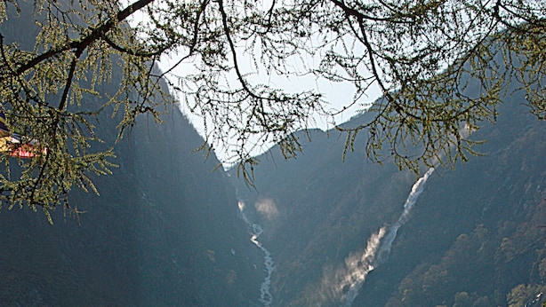 A row of small cabins with a mountain backdrop, a river running through the valley, and a flag on one of the cabins. - Eidfjord Gjestgiveri (Eidfjord)
