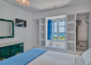 A bedroom with a bed, a large mirror, a wardrobe, a window with a view of the sea, and a built-in shower. - Blue Dolphin Antiparos Villas and Suites (Antiparos)