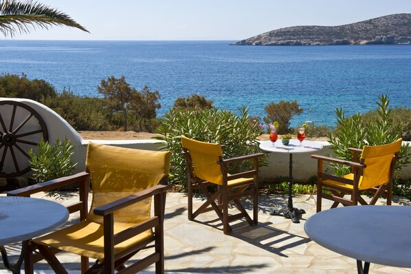 A terrace with wooden chairs and tables overlooking a coastal view. - Blue Dolphin Antiparos Villas and Suites (Antiparos)