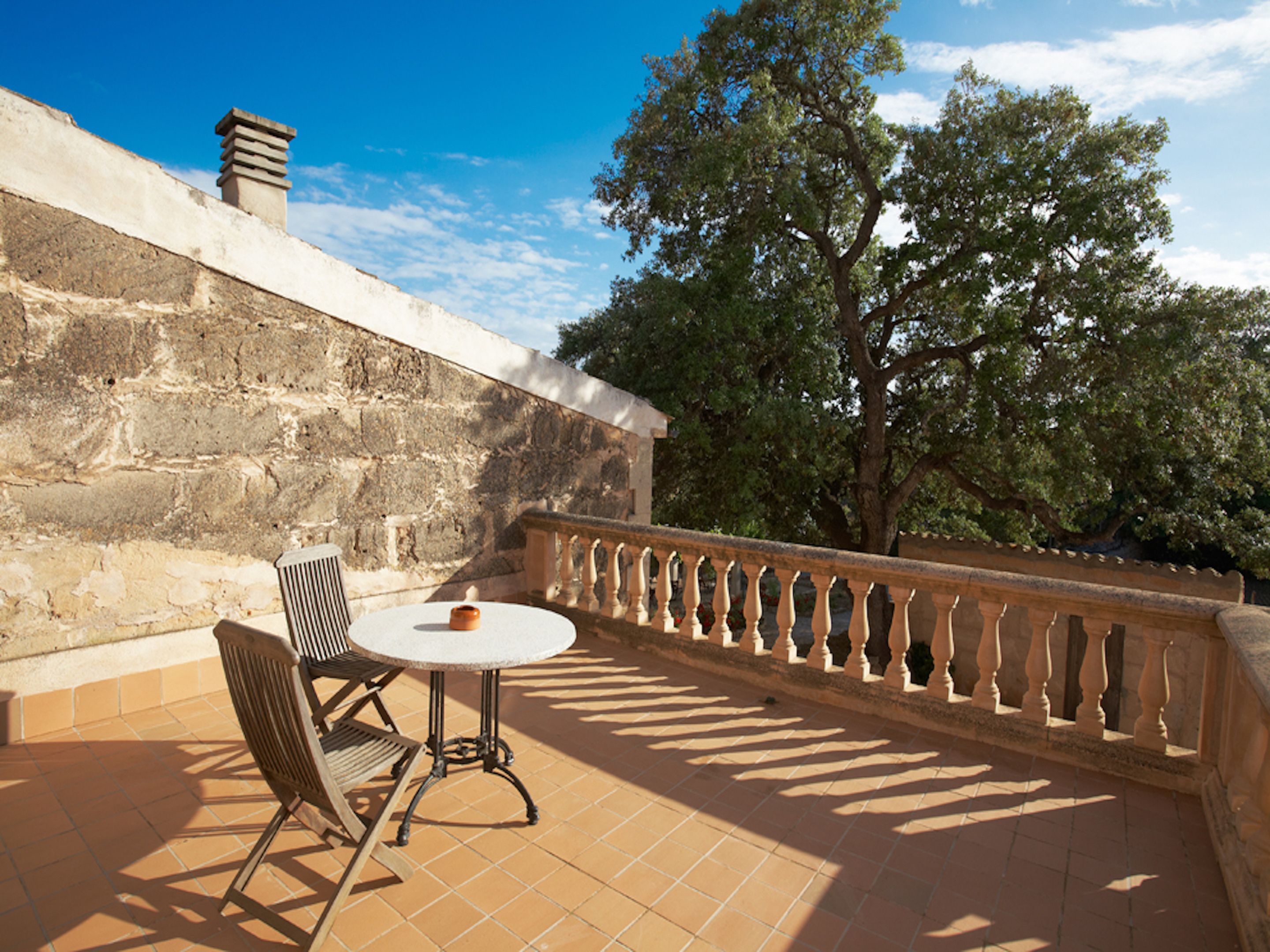 Eine Terrasse mit einer Steinmauer, einem Tisch, einem Stuhl und einem Geländer.