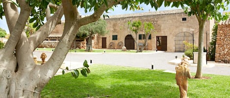 Un patio con un edificio de piedra, una estatua y un árbol que da sombra.