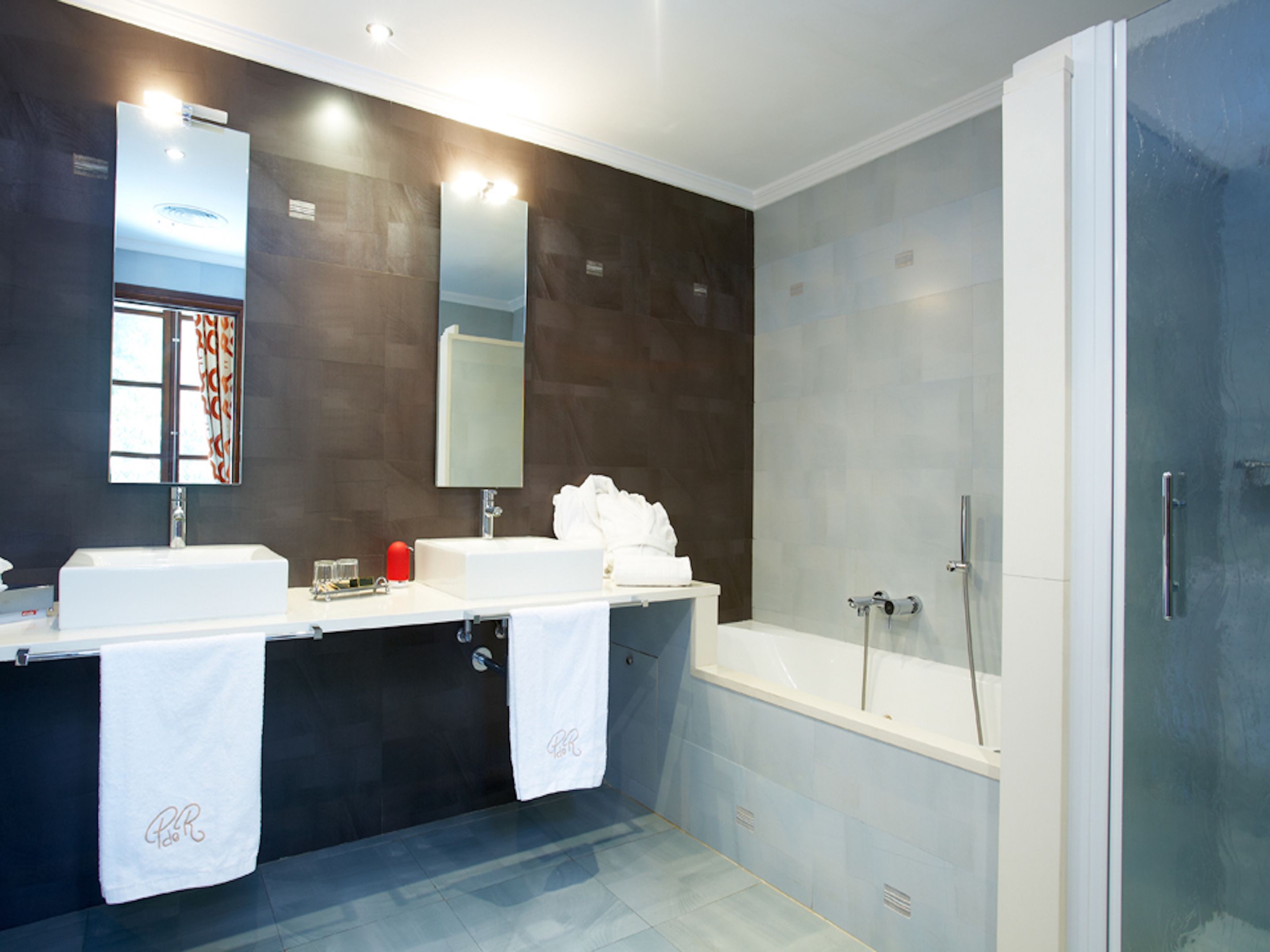 A modern bathroom with two sinks, a large mirror, and a walk-in shower.