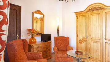 A room with two upholstered armchairs, a wooden wardrobe, a television on a wooden cabinet, and a glass table.