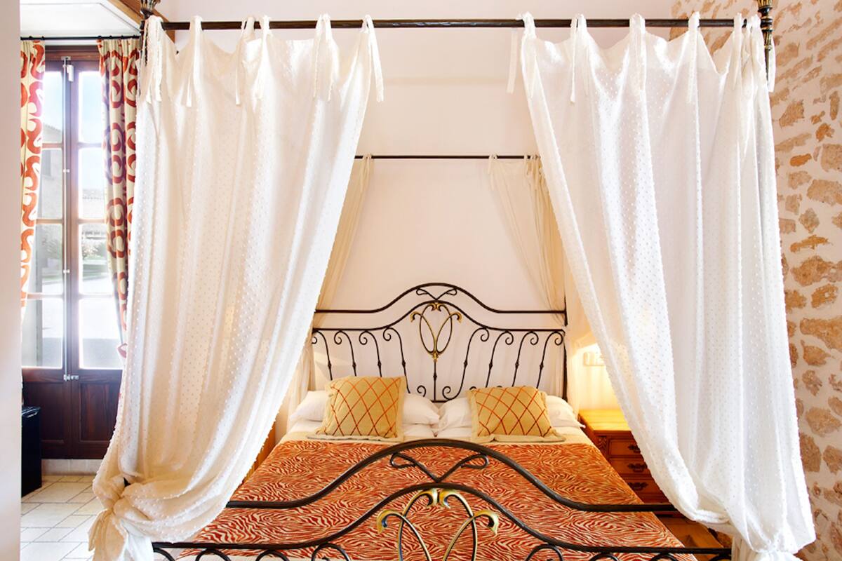 A bed with a metal frame, white curtains, and a patterned bedspread.