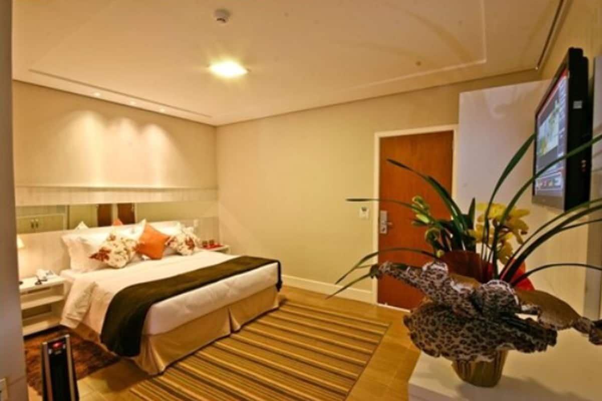 Une chambre d’hôtel avec un lit, une table de chevet, une lampe et une plante décorative.