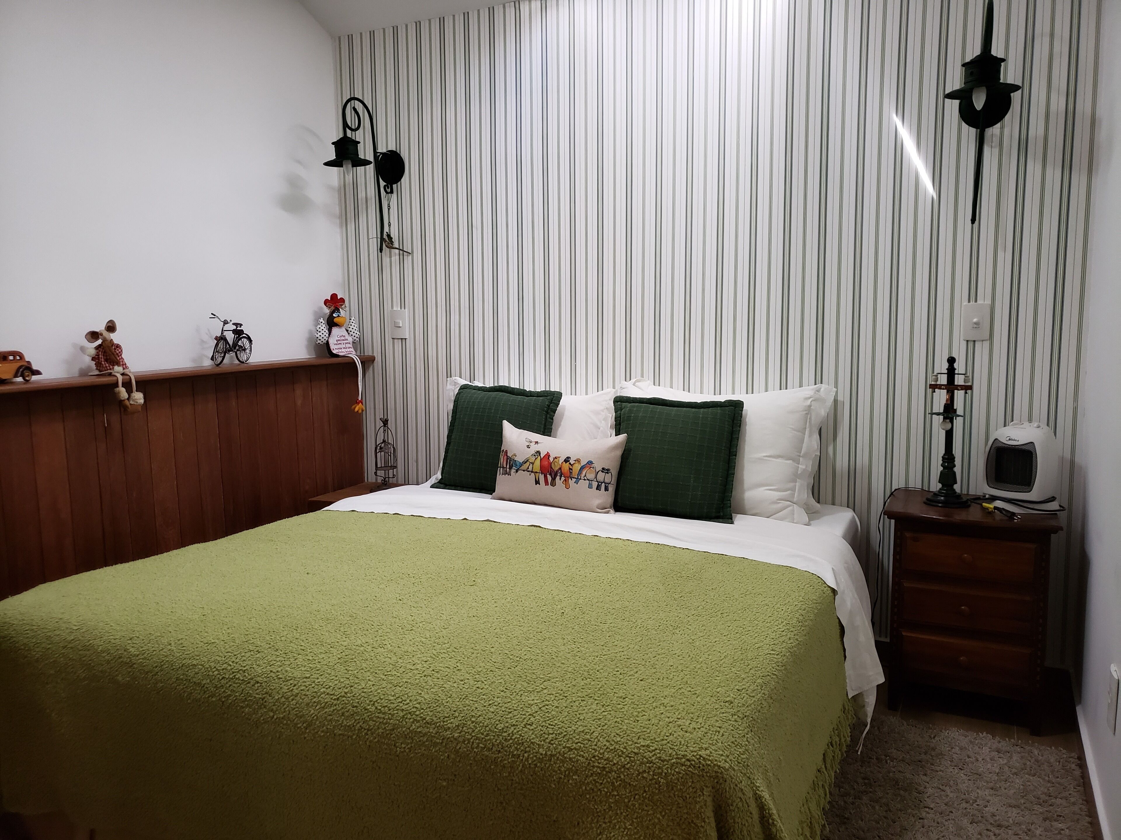 A neatly arranged bedroom with a bed, a nightstand, a wall-mounted lamp, and a striped curtain.
