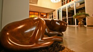 Eine große bronzene Skulptur eines liegenden Tieres in einer Lobby mit einem Chandelier und großen Fenstern.