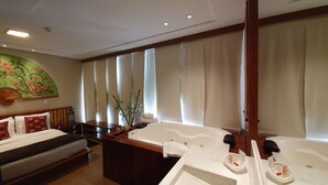 Ein Hotelzimmer mit Bett, Sitzgelegenheit, Badewanne und großem Fenster mit Vorhängen.
