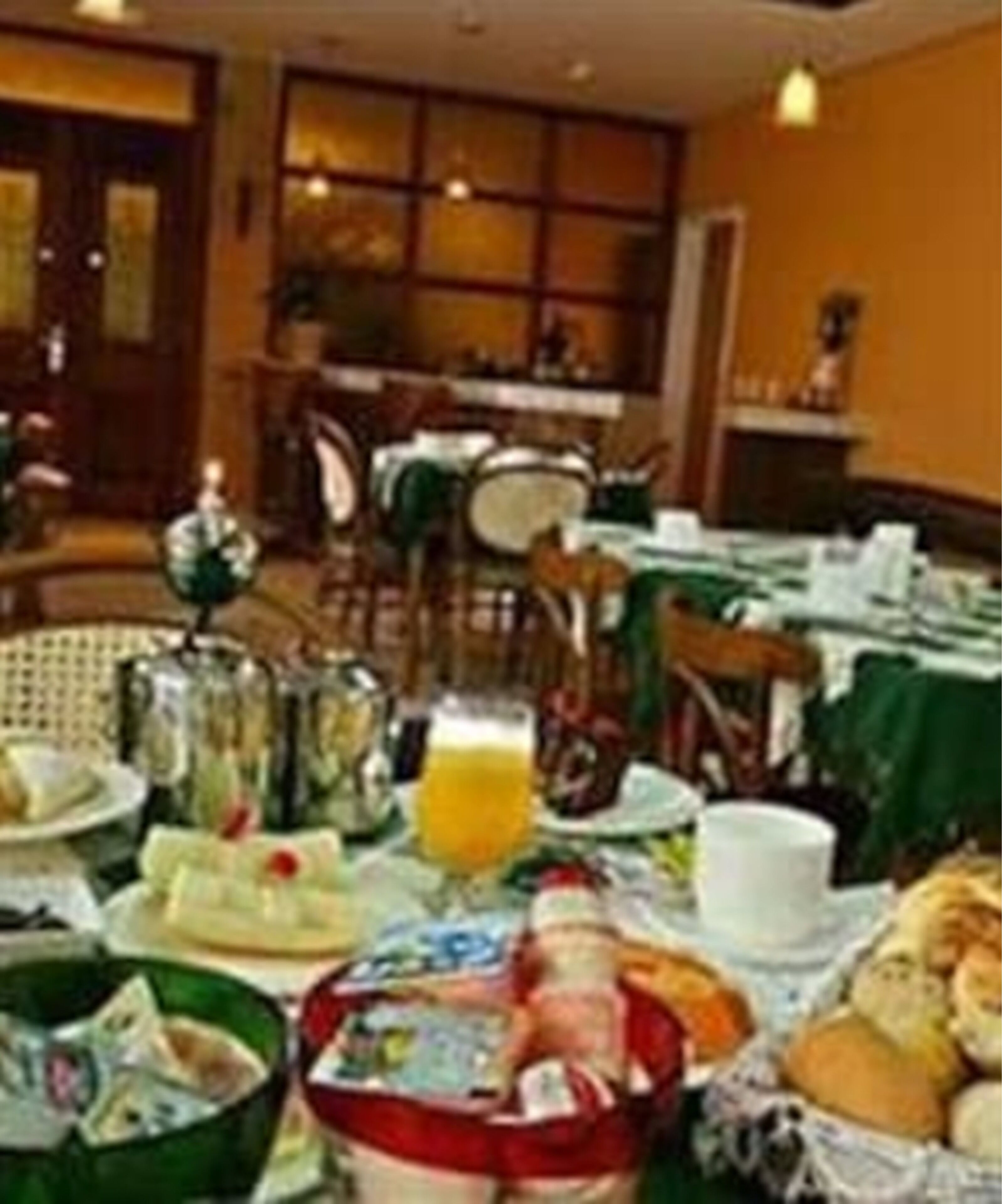 Un comedor con mesas dispuestas para el desayuno, incluyendo platos, tazas y un vaso de jugo de naranja.