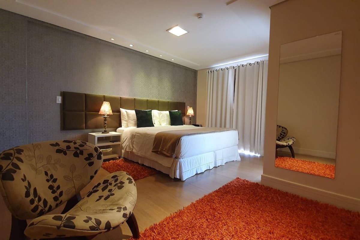 Une chambre d’hôtel moderne avec un grand lit, une chaise, une table de chevet et un miroir.