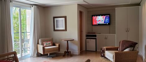 A hotel room with a bed, two chairs, a small table, a TV, a mini-fridge, and a wardrobe.