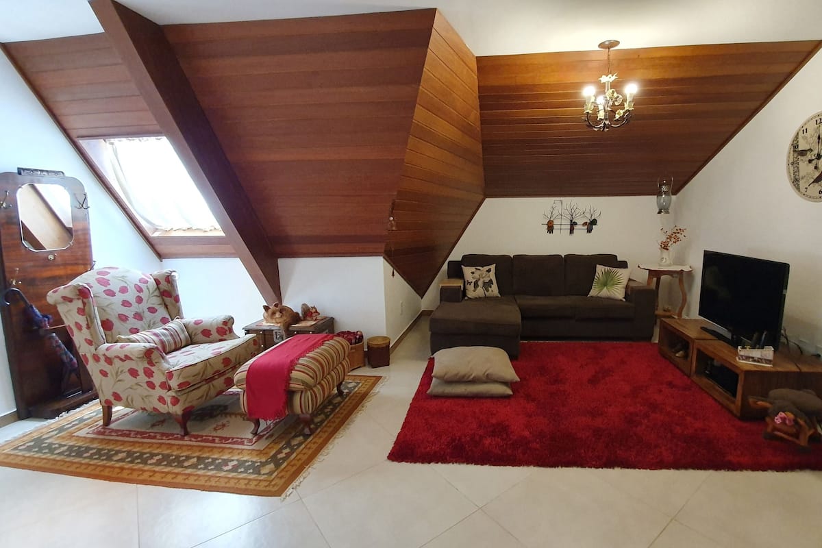 Un salon chaleureux avec un plafond en pente, un canapé, un tapis rouge, un téléviseur et une horloge au mur.