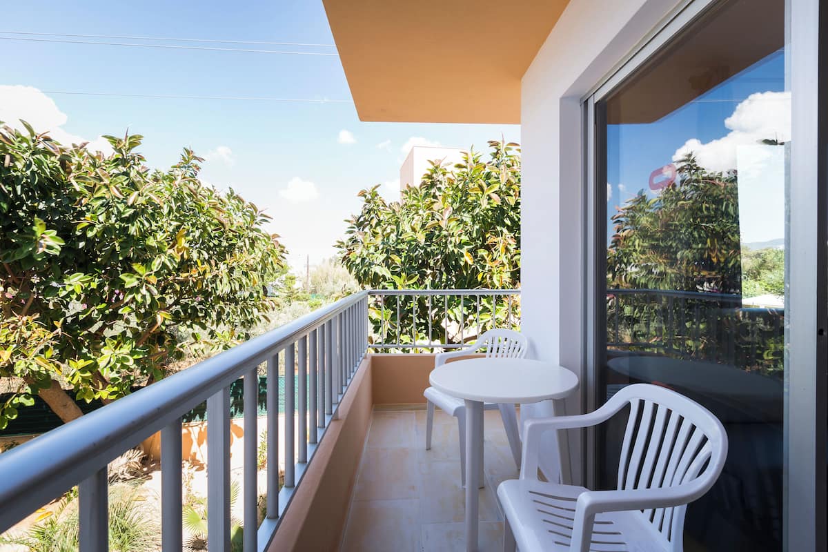 Ein Balkon mit einem weißen Tisch und Stühlen, umgeben von Grünpflanzen und einem klaren Himmel.