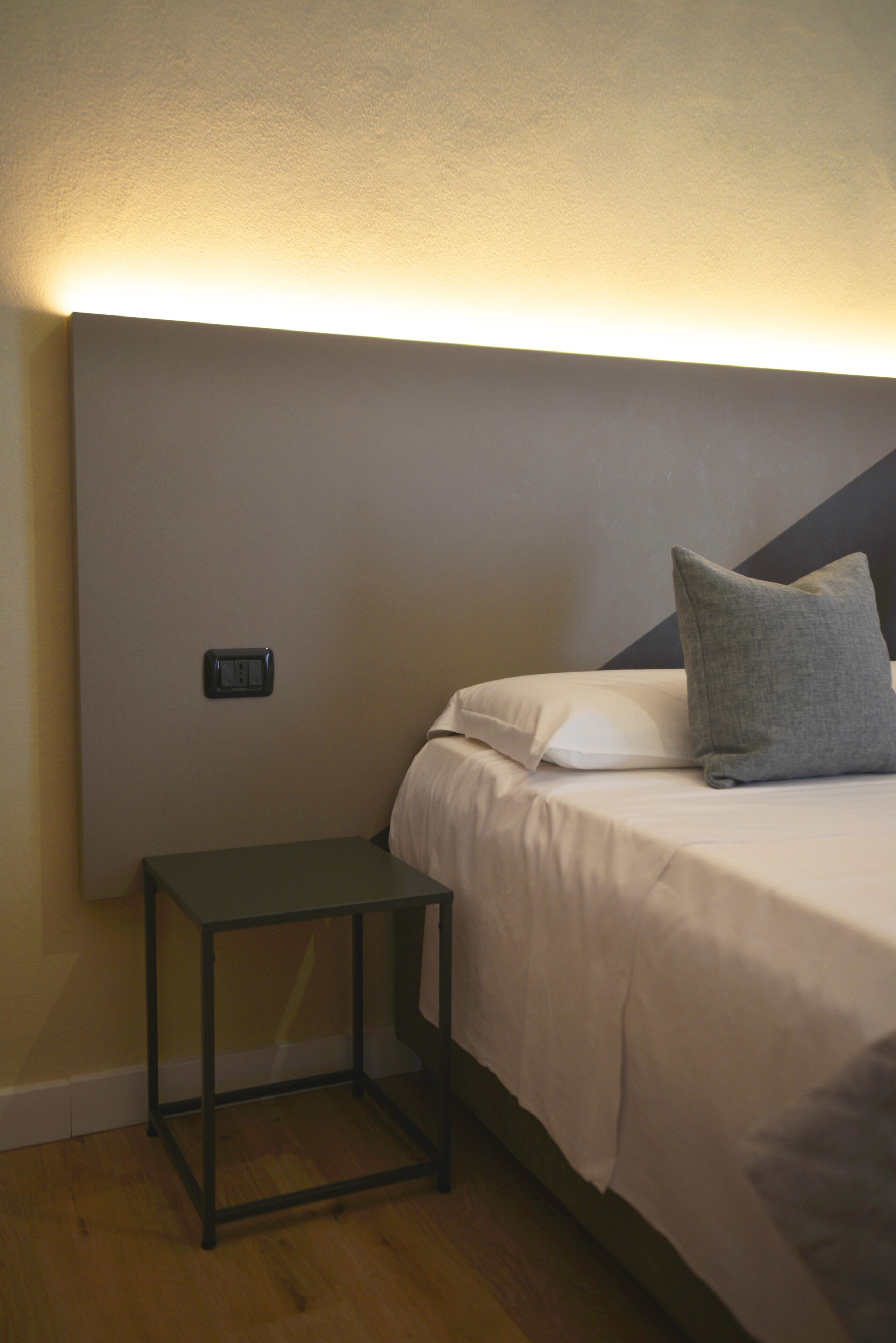 Un lit bien fait, avec un oreiller gris, une table de chevet et un luminaire fixé au mur.