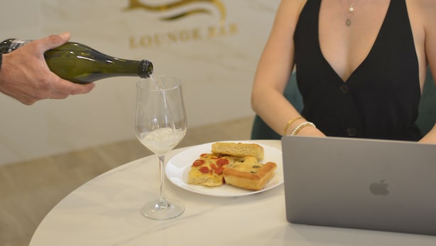 Una persona serviendo una bebida en un vaso sobre una mesa con una computadora portátil y un plato de comida.