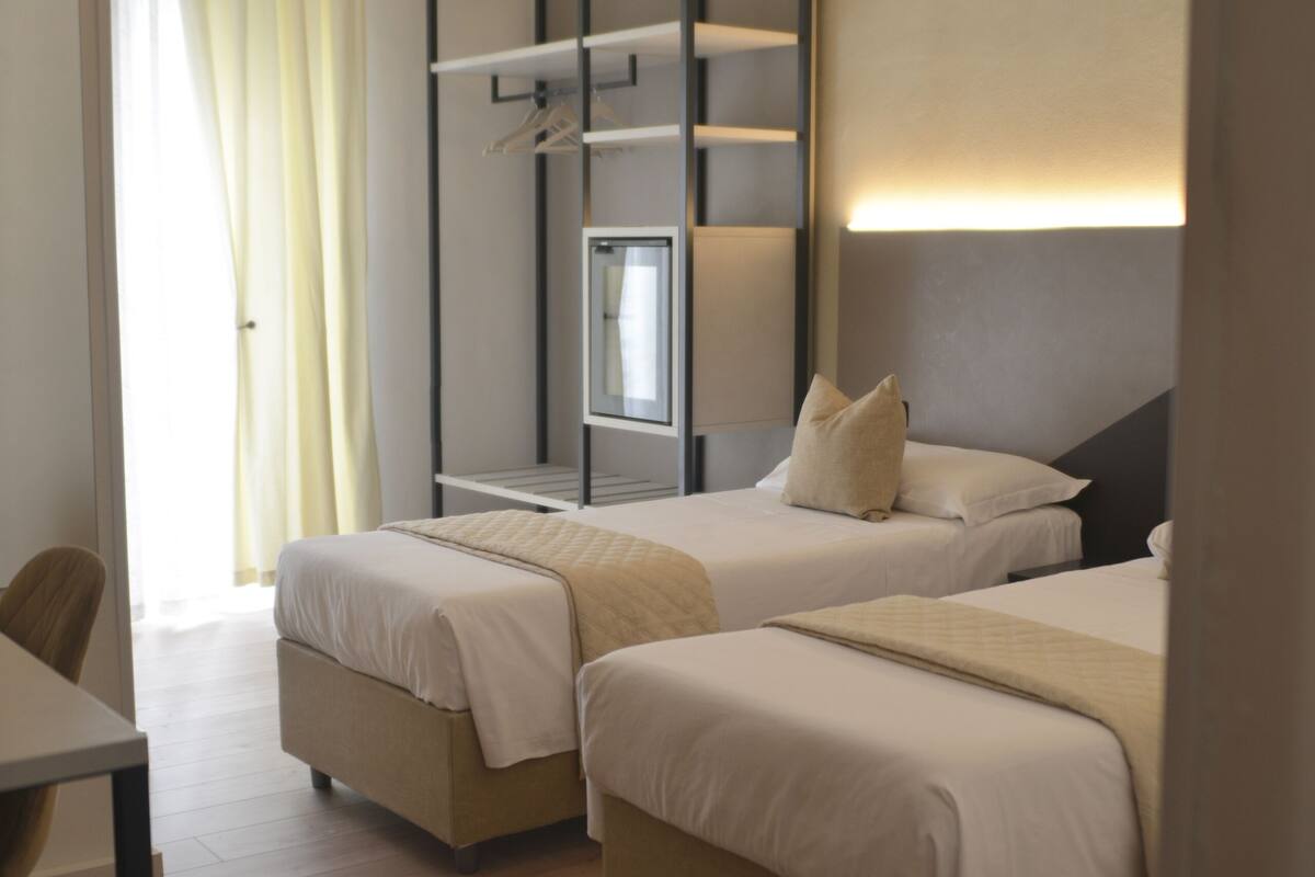 Une chambre d’hôtel avec deux lits, un bureau et une fenêtre avec des rideaux.