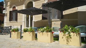 Mobiliario exterior con sombrillas, plantas en macetas y bicicletas estacionadas frente a una fachada.