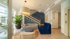 A modern interior with a staircase, a sofa, a blue armchair, and a potted plant. - Mar Calma Hotel (Pollenca)