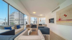 A modern living room with large windows, a sofa set, a coffee table, and a painting on the wall. - Mar Calma Hotel (Pollenca)