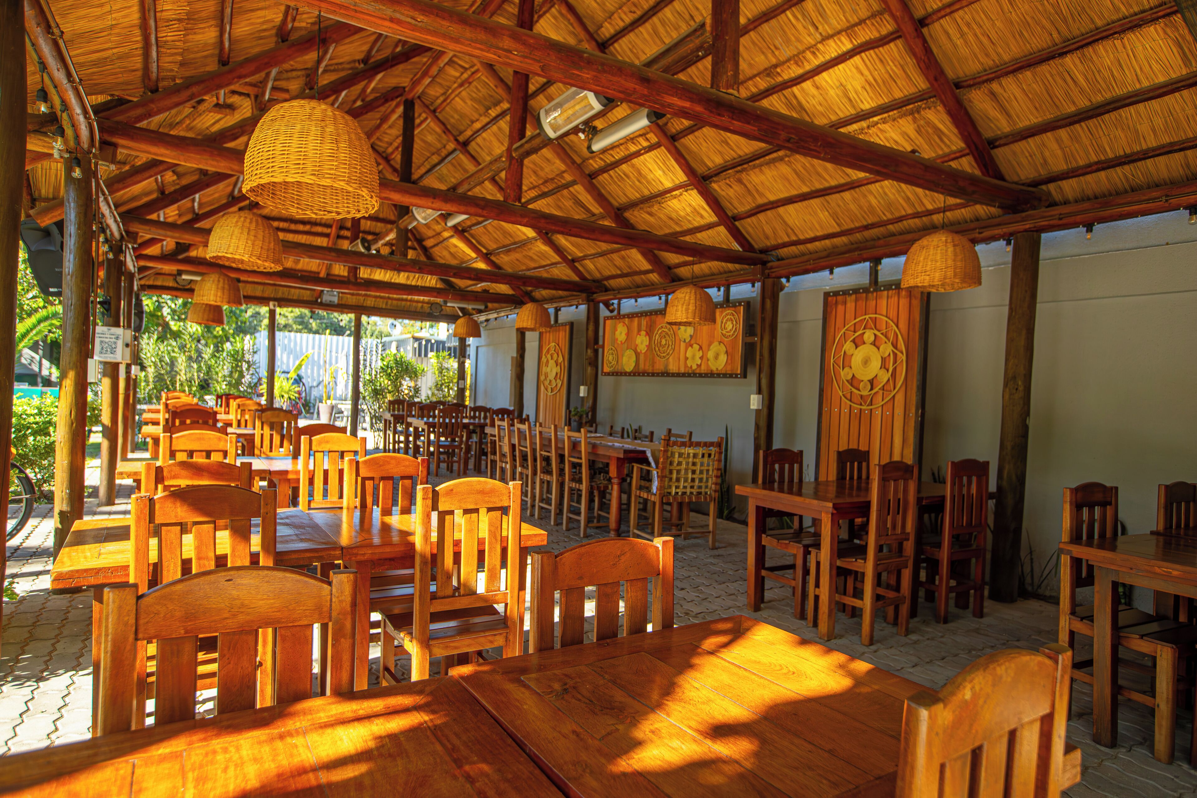 An outdoor restaurant with wooden tables and chairs, thatched roof, and hanging baskets.