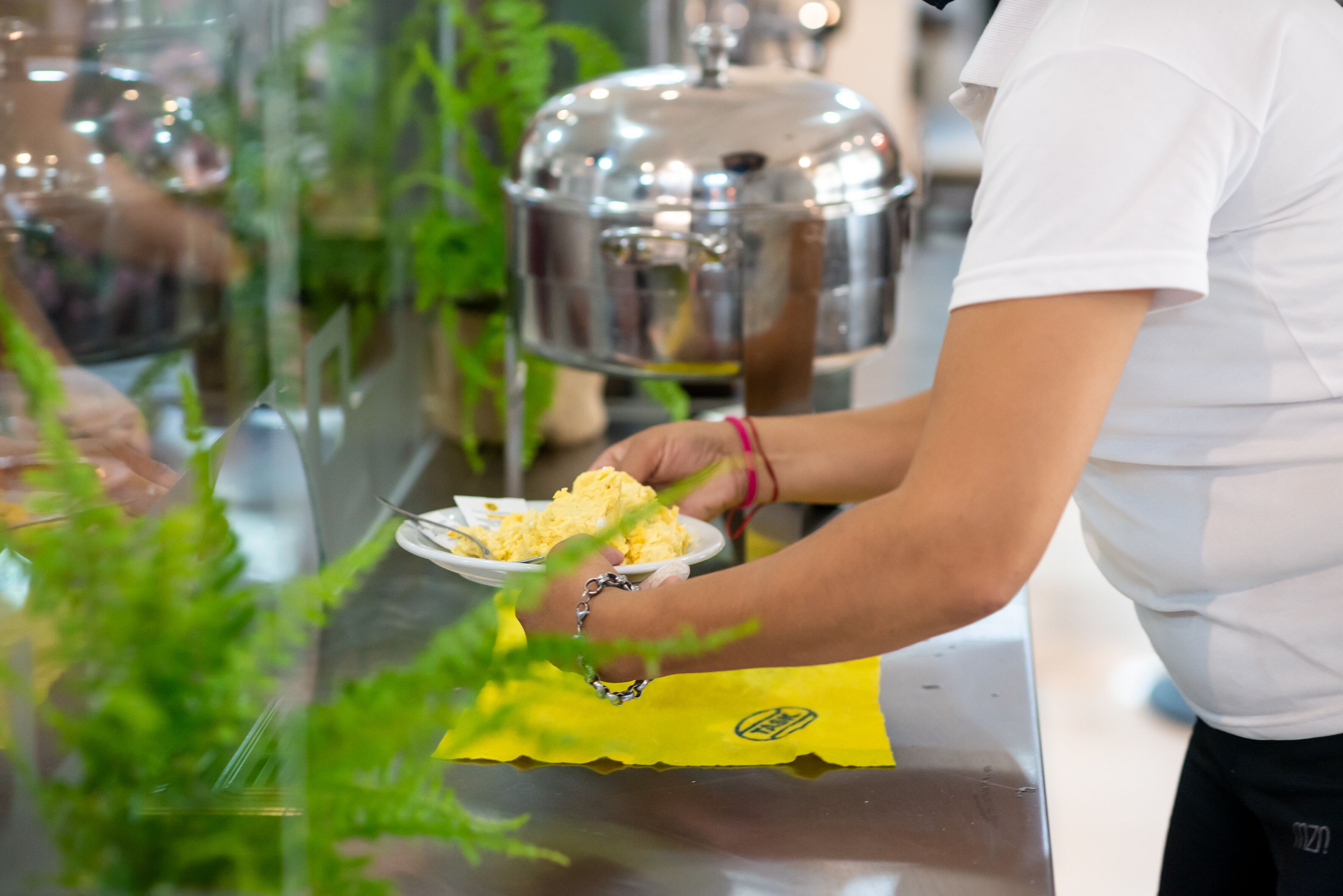 A person serving food at a buffet with a large metal pot in the background.