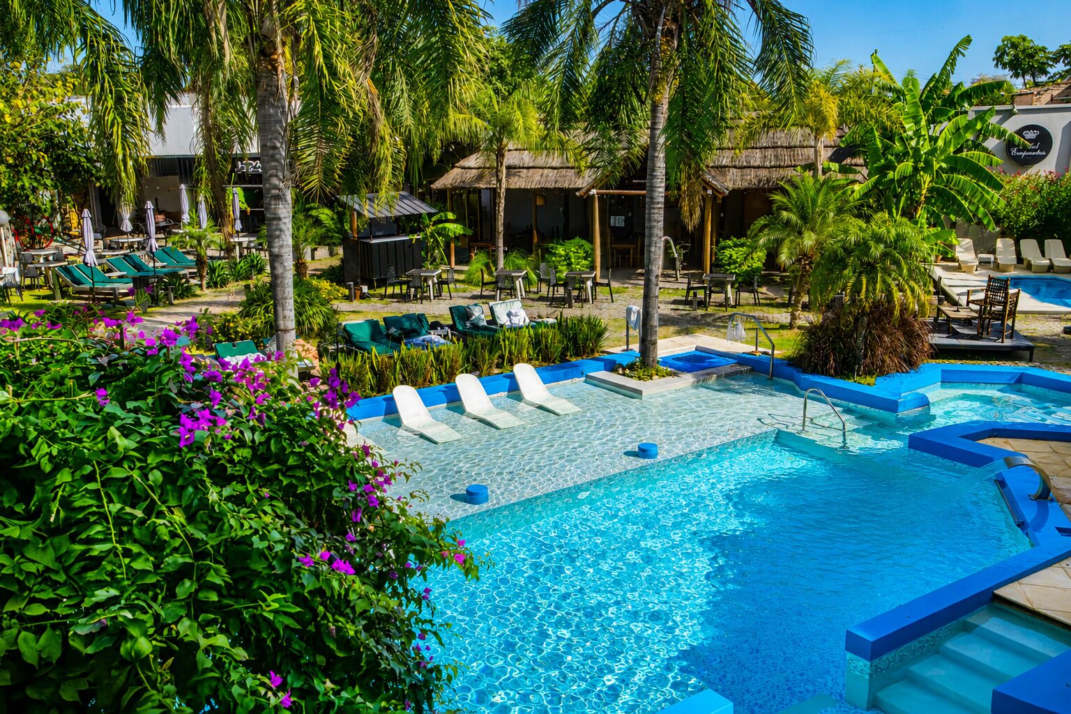 Zona de piscina con sillones reclinables, bañera de hidromasaje y vegetación tropical.