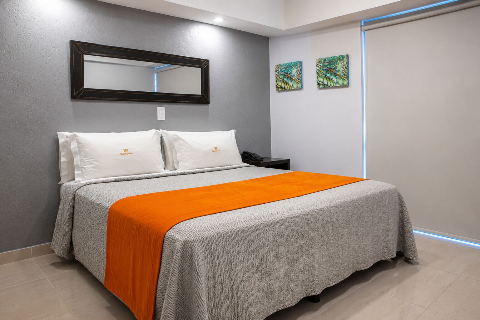 A hotel room with a bed, a nightstand, a telephone, and two wall-mounted paintings.