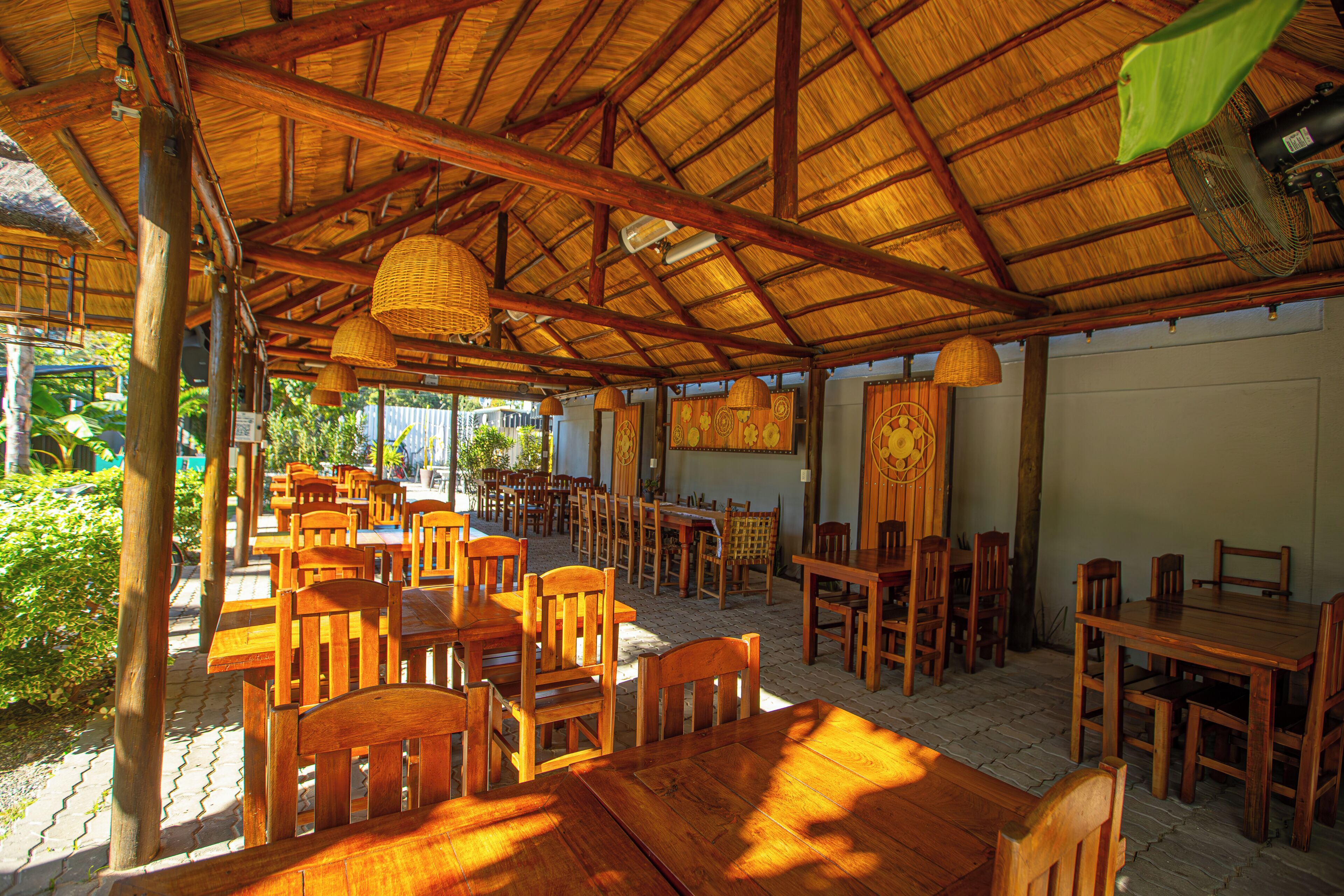 Un comedor interior con mesas y sillas de madera, techo de paja y cestas colgantes.