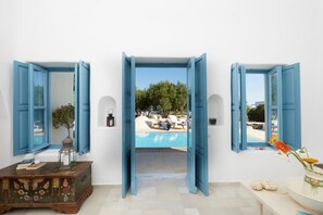 A room with a view of a swimming pool, a wooden chest of drawers, and a vase with flowers. - Black Rose Suites (Santorini)