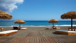 Una spiaggia con lettini di legno e ombrelloni di paglia, una passerella in legno e l'oceano sullo sfondo.