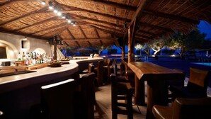Area bar all'aperto con tetto di paglia, mobili in legno e vista sulla spiaggia al crepuscolo.