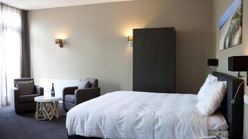 Een hotelkamer met een groot bed, twee fauteuils, een klein rond tafeltje en een kledingkast.