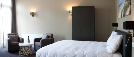 A hotel room with a large bed, two armchairs, a small round table, and a wardrobe.