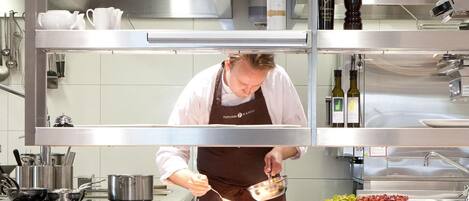 Een kok in een professionele keuken, met roestvrijstalen apparatuur, een pan op het aanrecht en een fles wijn in de kast.
