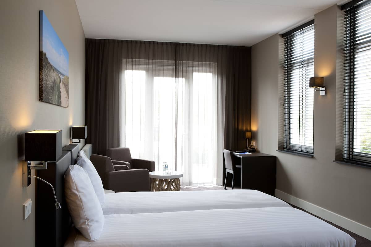 Une chambre d’hôtel avec un grand lit, un bureau, deux chaises, une petite table et un tableau au mur.
