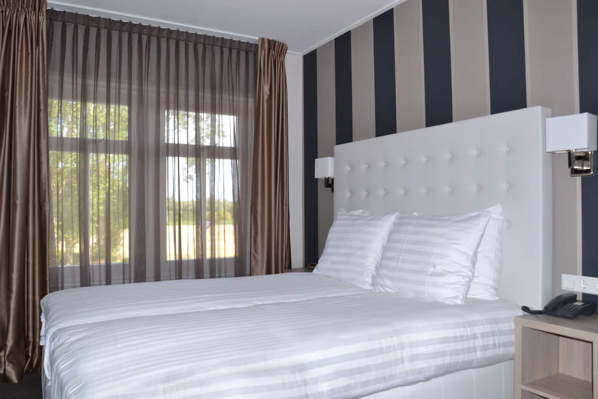 Une chambre d’hôtel avec un grand lit, une lampe de chevet, un téléphone et une vue sur les arbres par la fenêtre.
