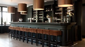 Een bar met een lange toonbank, meerdere krukken en hangende lampen.