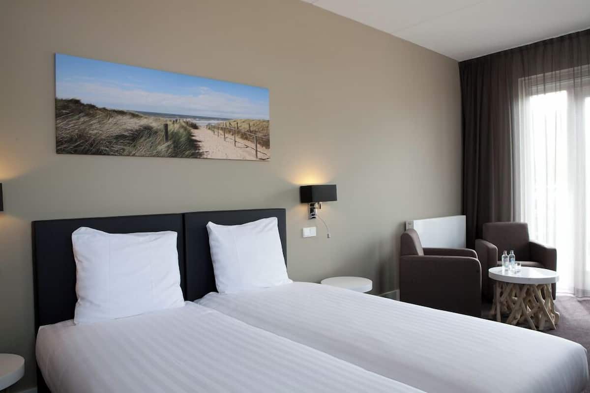 Une chambre d’hôtel avec un grand lit, deux tables de chevet, une chaise, une table ronde et une décoration murale sur le thème de la plage.