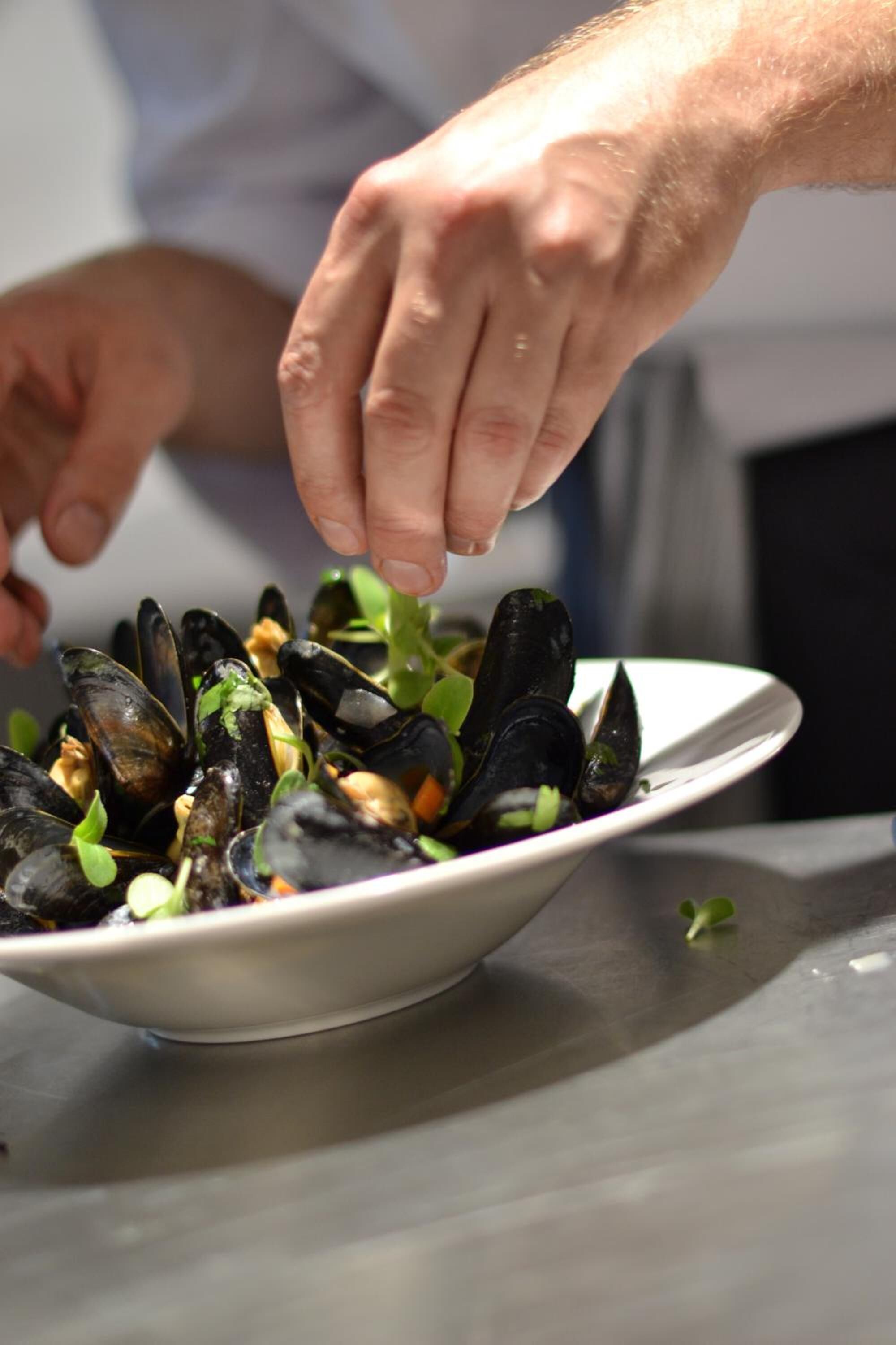 A person serving mussels from a white bowl.