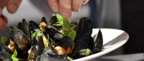 Una persona sirviendo mejillones desde un tazón blanco.