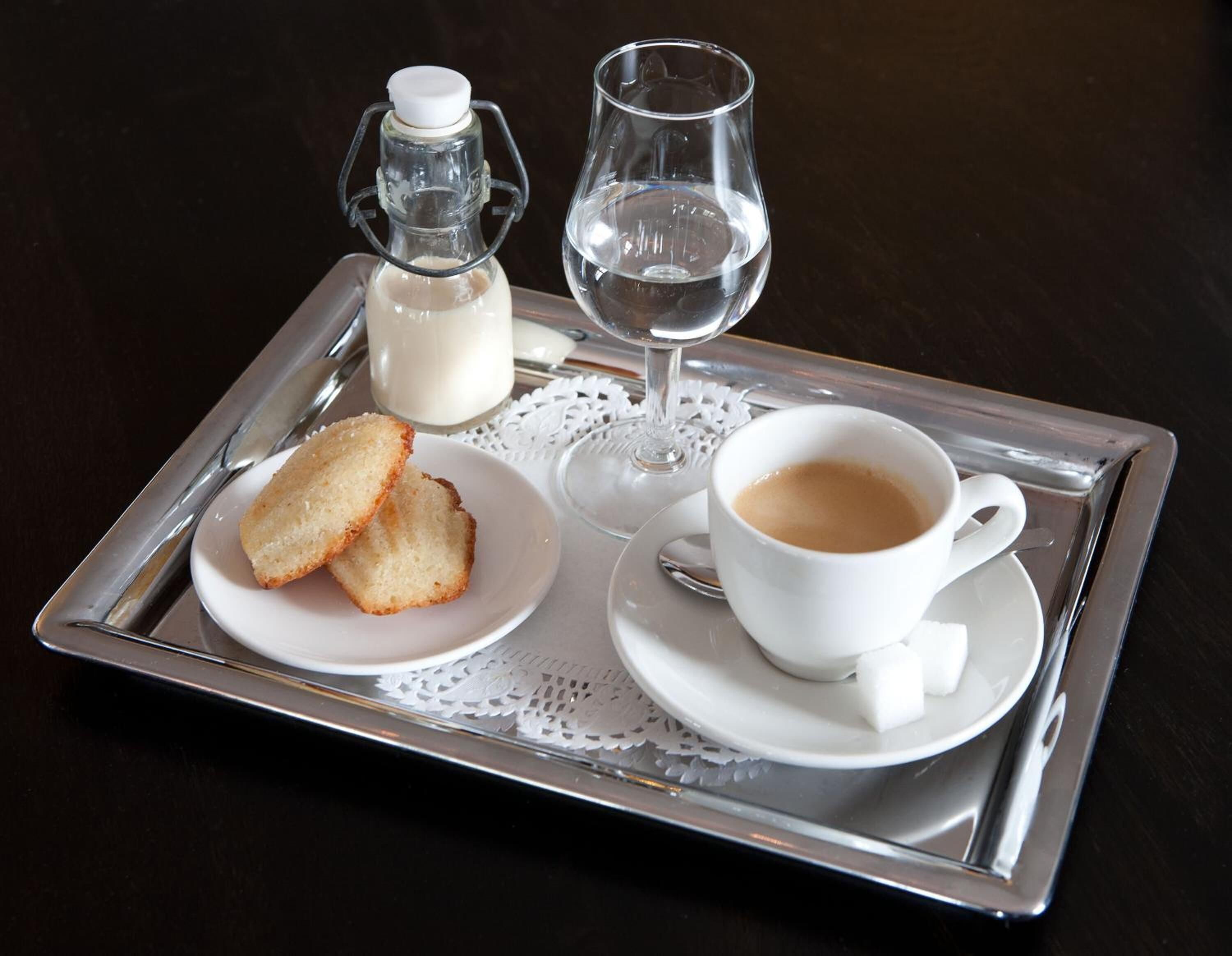 A tray with a glass of water, a cup of coffee, a bottle of milk, and two slices of bread.