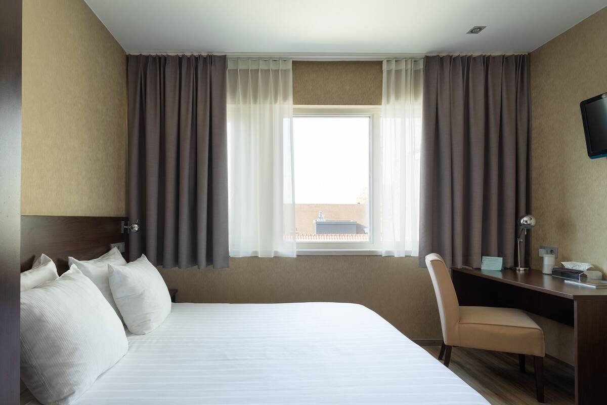 A hotel room with a large bed, a desk, a chair, and a television on the wall.