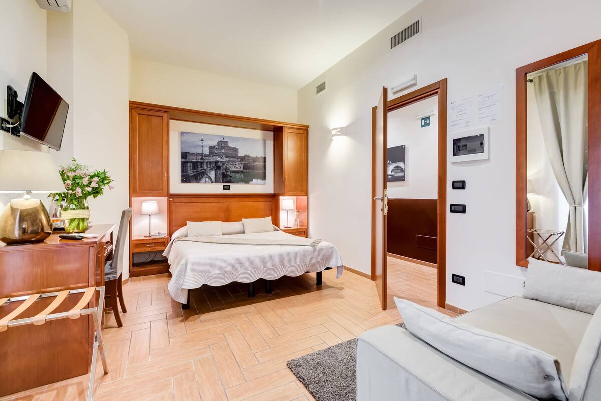 A hotel room with a bed, bedside tables, a desk, a chair, a TV, a picture on the wall, and a door.