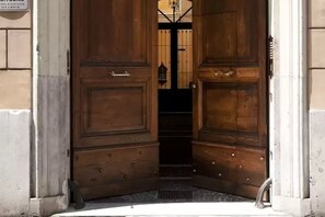 Een houten dubbele deur met een metalen handgreep, leidend naar een donker interieur.
