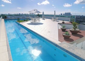 A rooftop pool with clear blue water, surrounded by lounge chairs and umbrellas, and a city skyline in the background.