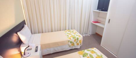 A hotel room with two single beds, a desk with a chair, a TV on a shelf, and a wardrobe.