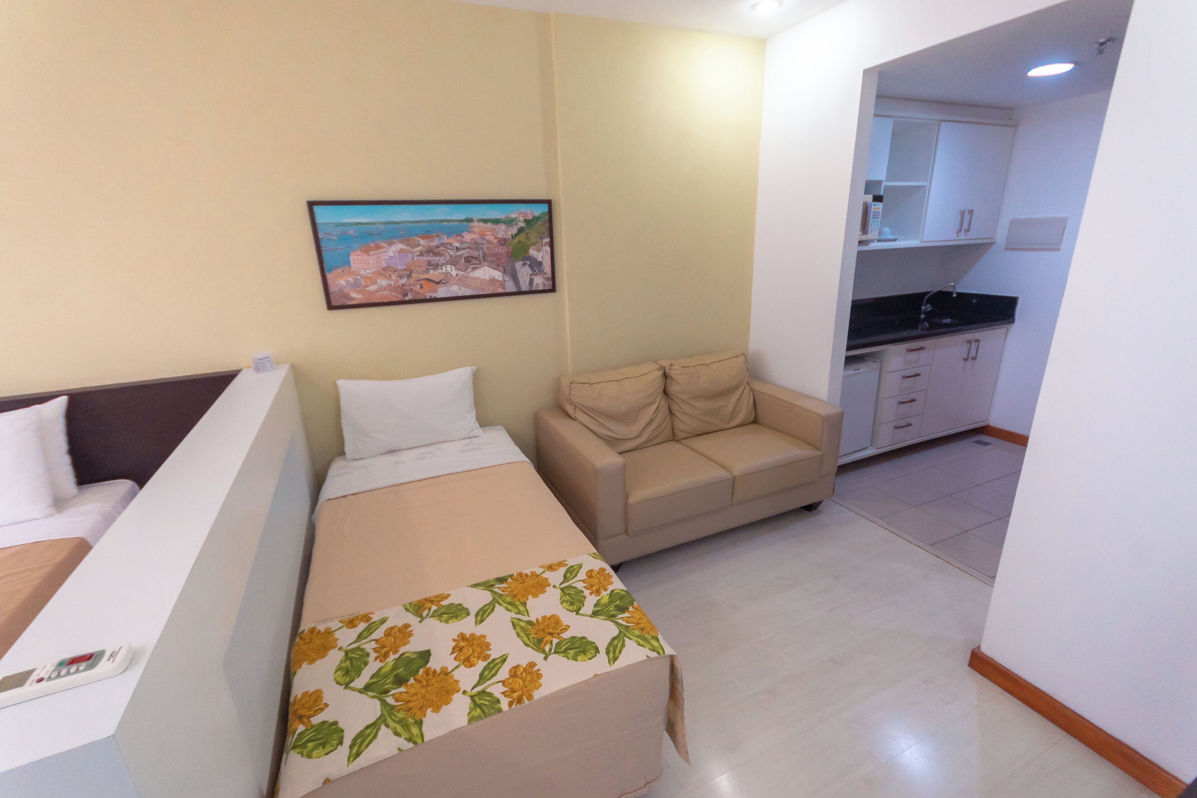 Habitación de hotel pequeña con cama, sofá, kitchenette y un cuadro en la pared.