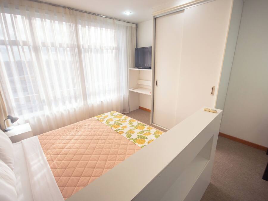 A bedroom with a bed, a TV on a shelf, a wardrobe, and a window with curtains.