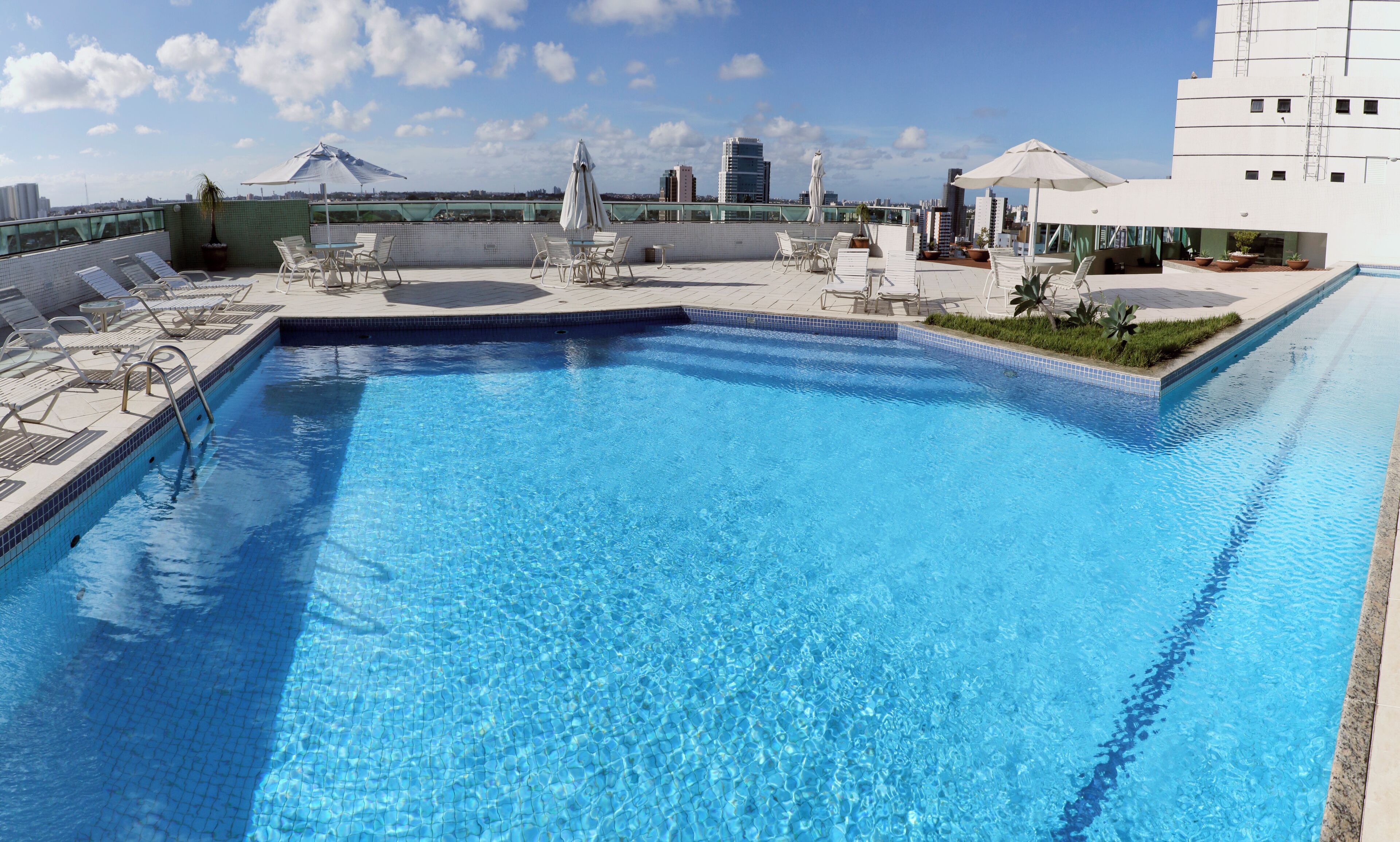 Ein Dachpool mit klarem, blauem Wasser, umgeben von Liegestühlen und Sonnenschirmen.